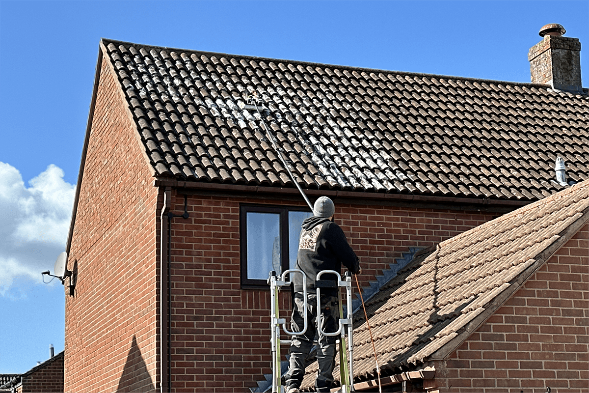 Professional applying biocide moss and lichen treatment to roof tiles from scaffold
